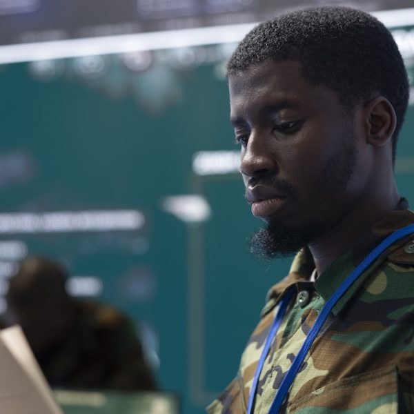 Army soldier reading a new defense operation case file in military headquarters, using reconnaissance CCTV footage on a big screen. Recruit tracking location of deployed troops. Close up.