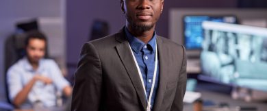 Waist up portrait of black businessman wearing suit while standing in high tech secutrity office, copy space